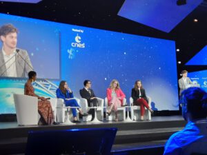 Fünf Teilnehmerinnen und Teilnehmer einer Podiumsdiskussion auf einer Bühne, auf weißen Stühlen und vor blauem Hintergrund mit Sternen